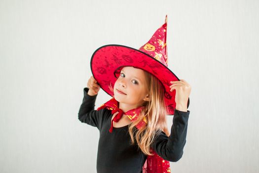 Celebrating halloween. A little cheerful girl plays and has fun in a carnival witch costume: a cloak and a hat.