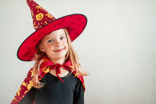 Celebrating halloween. A little cheerful girl plays and has fun in a carnival witch costume: a cloak and a hat.