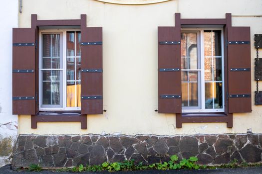 Two Windows with wooden shutters on the pink facade of a residential building.