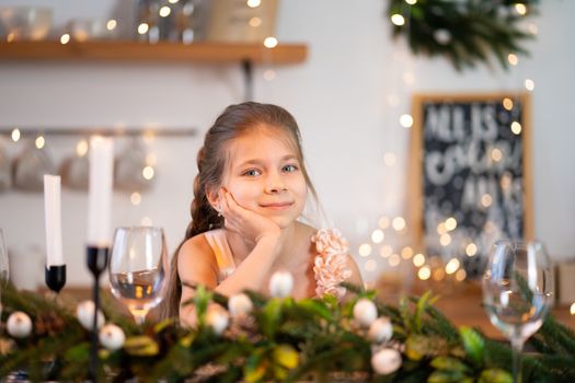 Little girl is bored sitting at the festive table on Christmas night.