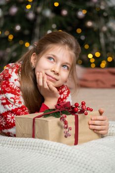 A little girl in pajamas early in the morning found a present from Santa under the tree. Christmas magic fairy tale. Happy childhood.