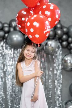 Little girl with red balloons celebrates her birthday.