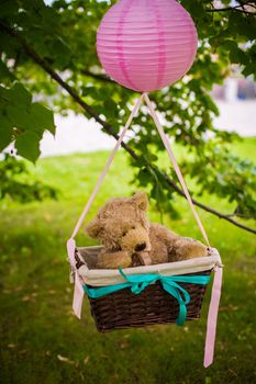 street decorations for a children's party. A basket with a teddy bear in a air balloon in a green park.