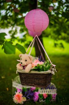 street decorations for a children's party. A basket with a teddy bear in a air balloon in a green park.