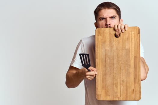 Man with a kitchen wooden board and with a shovel on a light background emotions white t-shirt model. High quality photo