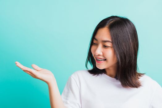 Portrait of Asian teen beautiful young woman smile have dental braces on teeth laughing she show hand side blank space, isolated on a blue background, Medicine and dentistry concept