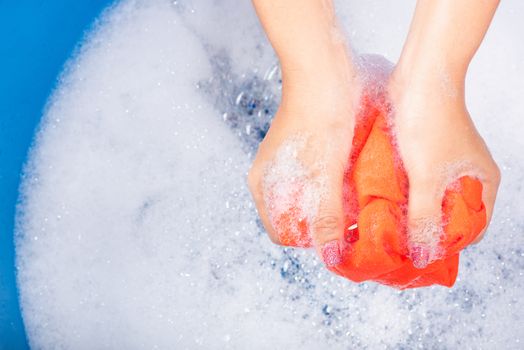 Closeup young Asian woman use hands washing color clothes in basin with detergent have soapy bubble water, studio shot background, laundry concept