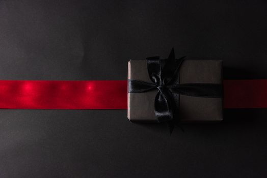 Black Friday Sale concept, Top view of gift box wrapped black paper and black bow ribbon press, studio shot on and having red ribbon across a dark background