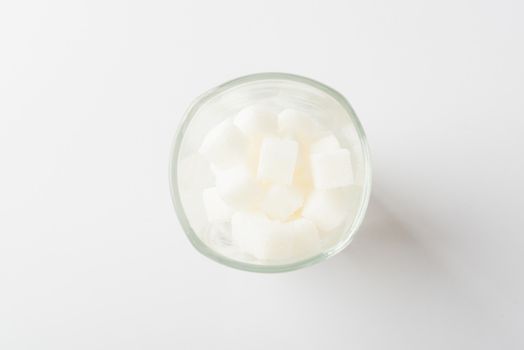 Top view glass full of white sugar cube sweet food ingredient, studio shot isolated on white background, health high blood risk of diabetes and calorie intake concept and unhealthy drink