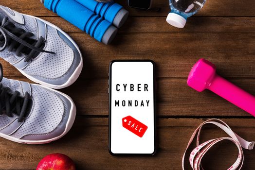 Cyber Monday sale concept with pair sports shoes, water, apple, jump rope and smartphone blank screen on wood table, Gray sneakers and accessories equipment in fitness GYM on wood table