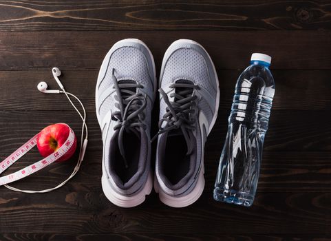 Pair sports shoes, headphones, apple and water bottle on black wood table background, Gray sneakers and accessories equipment in fitness GYM, Healthy workout active lifestyle diet concept