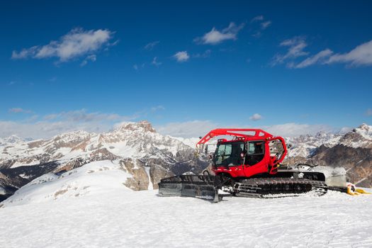 Red modern snowcat ratrack with snowplow snow grooming machine preparing ski slope piste hill at alpine skiing winter resort Cortina d'Ampezzo in Italy. Heavy machinery mountain equipment track vehicle