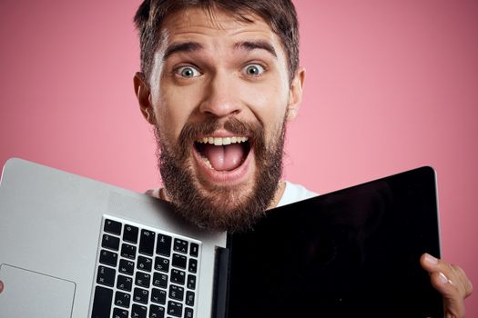 A man with an open laptop on a pink background white t-shirt gestures with his hands cropped view new technology keyboard monitor. High quality photo