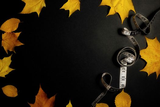 Autumn fallen leaves and measuring tape on black background