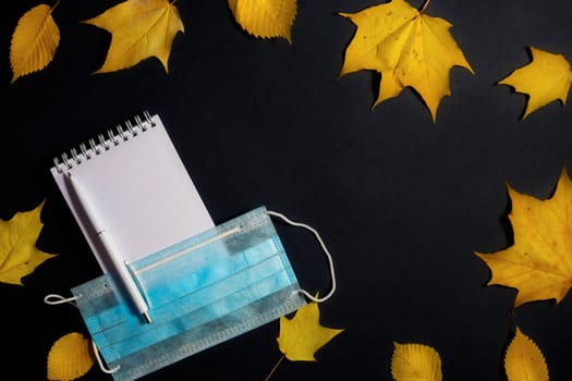 .Autumn fallen foliage, notebook and medical mask on black background.