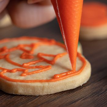 Close up of decorating cute Halloween pumpkin gingerbread cookies with frosting icing cream topping bag.