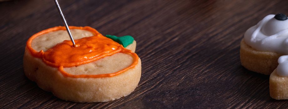 Close up of decorating cute Halloween pumpkin gingerbread cookies with frosting icing cream topping bag.