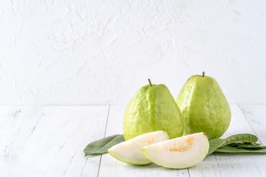 Delicious beautiful guava set with fresh leaves isolated on bright white wooden table background, close up.