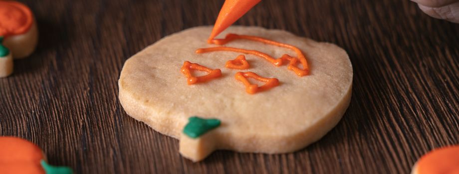 Close up of decorating cute Halloween pumpkin gingerbread cookies with frosting icing cream topping bag.