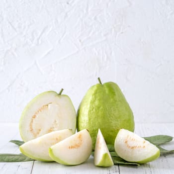 Delicious beautiful guava set with fresh leaves isolated on bright white wooden table background, close up.