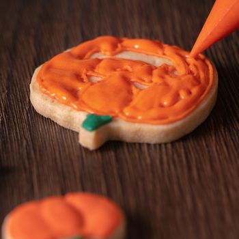 Close up of decorating cute Halloween pumpkin gingerbread cookies with frosting icing cream topping bag.