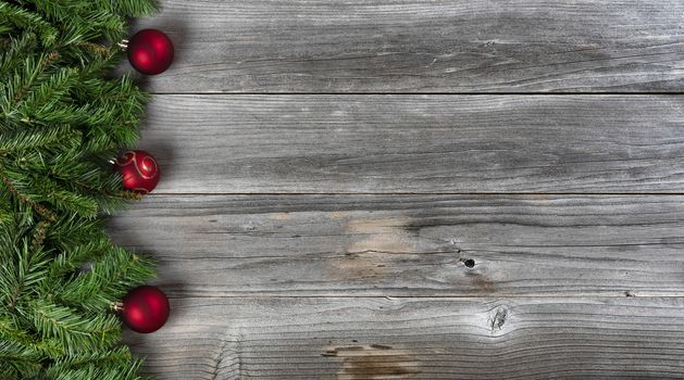 Merry Christmas and Happy New Year concept consisting of fir branches and red ball ornaments on left side of rustic wooden boards