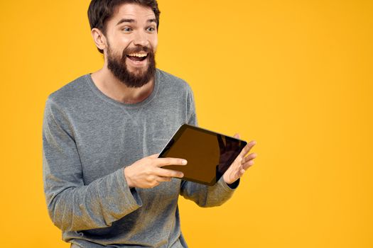 Emotional man with tablet in hands technology internet device lifestyle yellow background. High quality photo