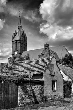 destroyed farm buildings and the tower of a historic gothic church in the village of Bledzew in Poland, black and white