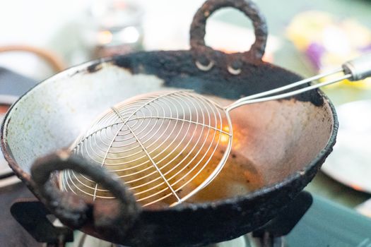 Empty old chipped deep frying pan with oil filled and a wire sieve placed ready to make and fry food . Shows the kitchen of a dhabha or a small street food vendor that is serving the masses of India