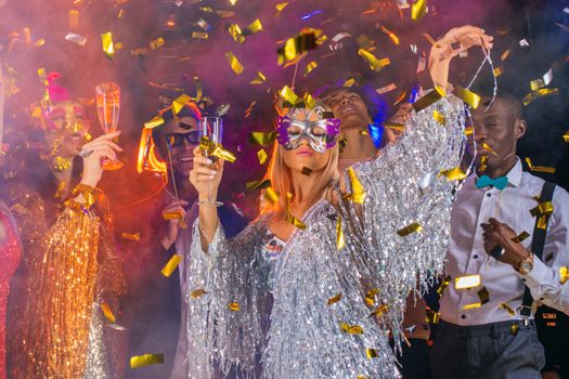 People having fun at 80s retro style party. People wearing costumes drinking champagne and dancing on dancefloor at nightclub in golden confetti