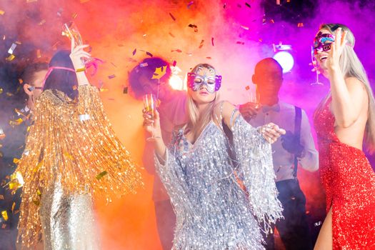 People having fun at 80s retro style party. People wearing costumes drinking champagne and dancing on dancefloor at nightclub in golden confetti