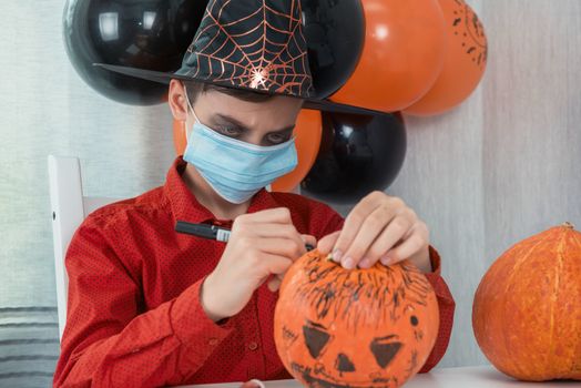 Teen boy in costume and face masks to protect against COVID-19 drawing a pumpkin for the Halloween celebration. Halloween carnival with new reality with pandemic concept.