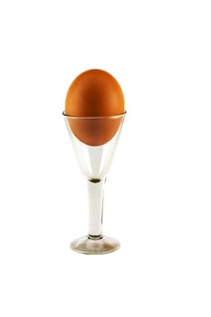 On a white background is a glass on a high leg with a chicken egg
