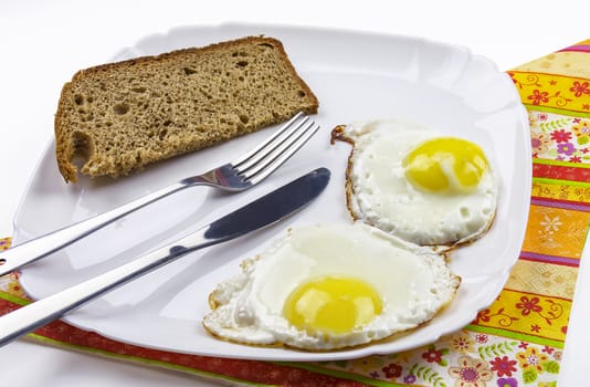 On the white plate is two fried eggs and a slice of black bread