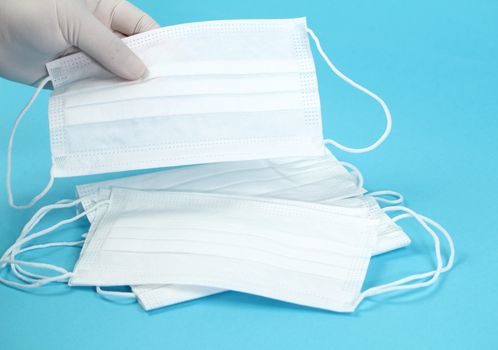 Hand with surgical gloves hanging Disposable Medical masks on blue background. Covid-19 and healthcare concept