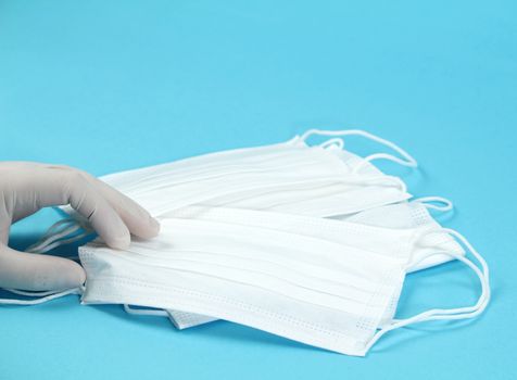 Hand with surgical gloves hanging Disposable Medical masks on blue background. Covid-19 and healthcare concept