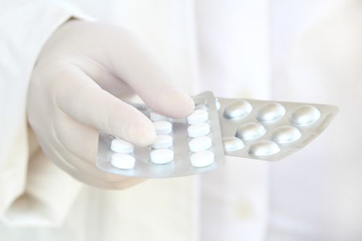 Male hand in white surgical glove holding pill blisters