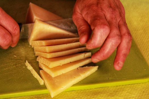 Hands slicing Manchego cheese slices in triangles on a green table