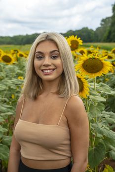 A gorgeous young blonde model poses outdoors in a field of sunflowers while enjoying a summers day