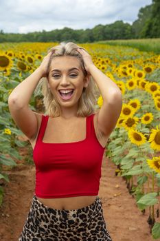 A gorgeous young blonde model poses outdoors in a field of sunflowers while enjoying a summers day