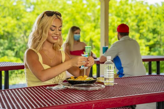 A gorgeous young blonde model enjoys her lunch outdoors while maintaining a safe distance from others during the Covid-19 pandemic
