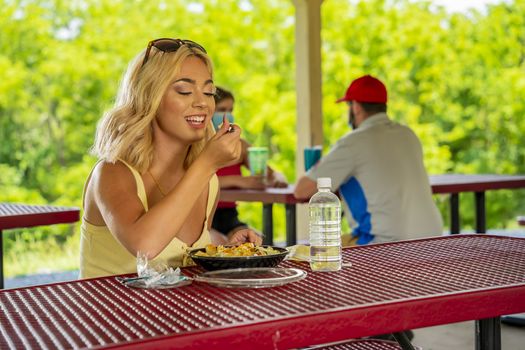 A gorgeous young blonde model enjoys her lunch outdoors while maintaining a safe distance from others during the Covid-19 pandemic