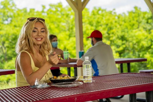 A gorgeous young blonde model enjoys her lunch outdoors while maintaining a safe distance from others during the Covid-19 pandemic