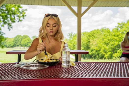 A gorgeous young blonde model enjoys her lunch outdoors while maintaining a safe distance from others during the Covid-19 pandemic