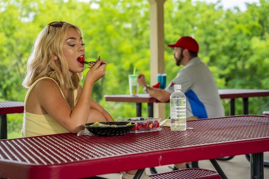A gorgeous young blonde model enjoys her lunch outdoors while maintaining a safe distance from others during the Covid-19 pandemic
