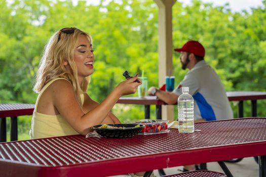 A gorgeous young blonde model enjoys her lunch outdoors while maintaining a safe distance from others during the Covid-19 pandemic