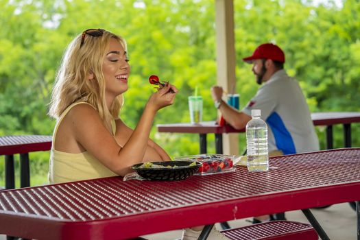 A gorgeous young blonde model enjoys her lunch outdoors while maintaining a safe distance from others during the Covid-19 pandemic