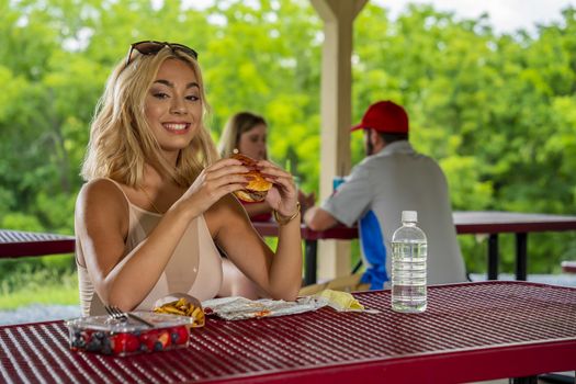 A gorgeous young blonde model enjoys her lunch outdoors while maintaining a safe distance from others during the Covid-19 pandemic