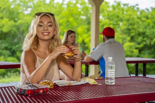 A gorgeous young blonde model enjoys her lunch outdoors while maintaining a safe distance from others during the Covid-19 pandemic