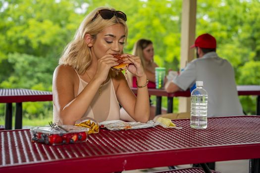 A gorgeous young blonde model enjoys her lunch outdoors while maintaining a safe distance from others during the Covid-19 pandemic